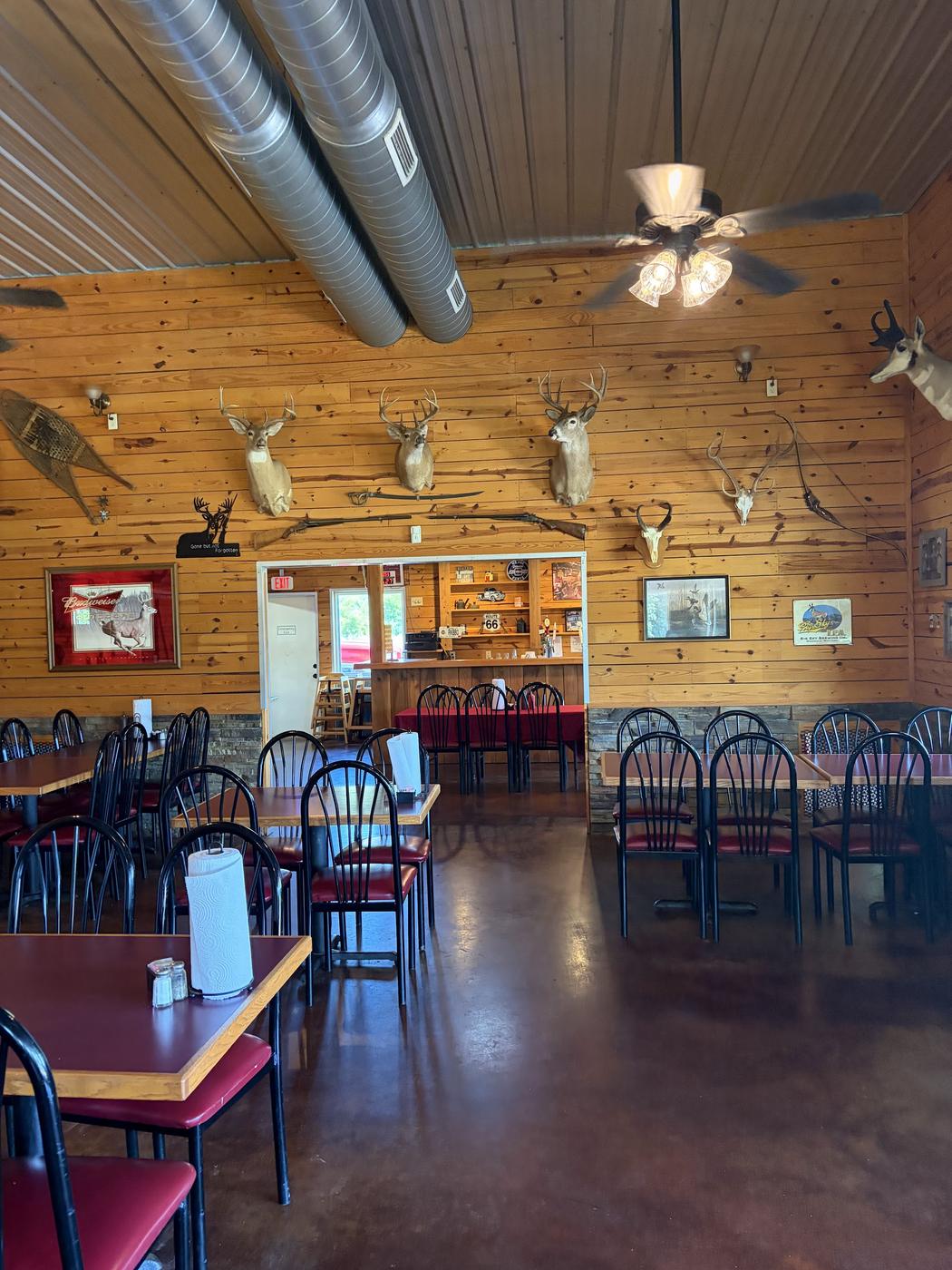 The dining room: knotty pine walls, mounted deer heads, snowshoes, an antique rifle over the doorway and red topped tables on a polished concrete floor.